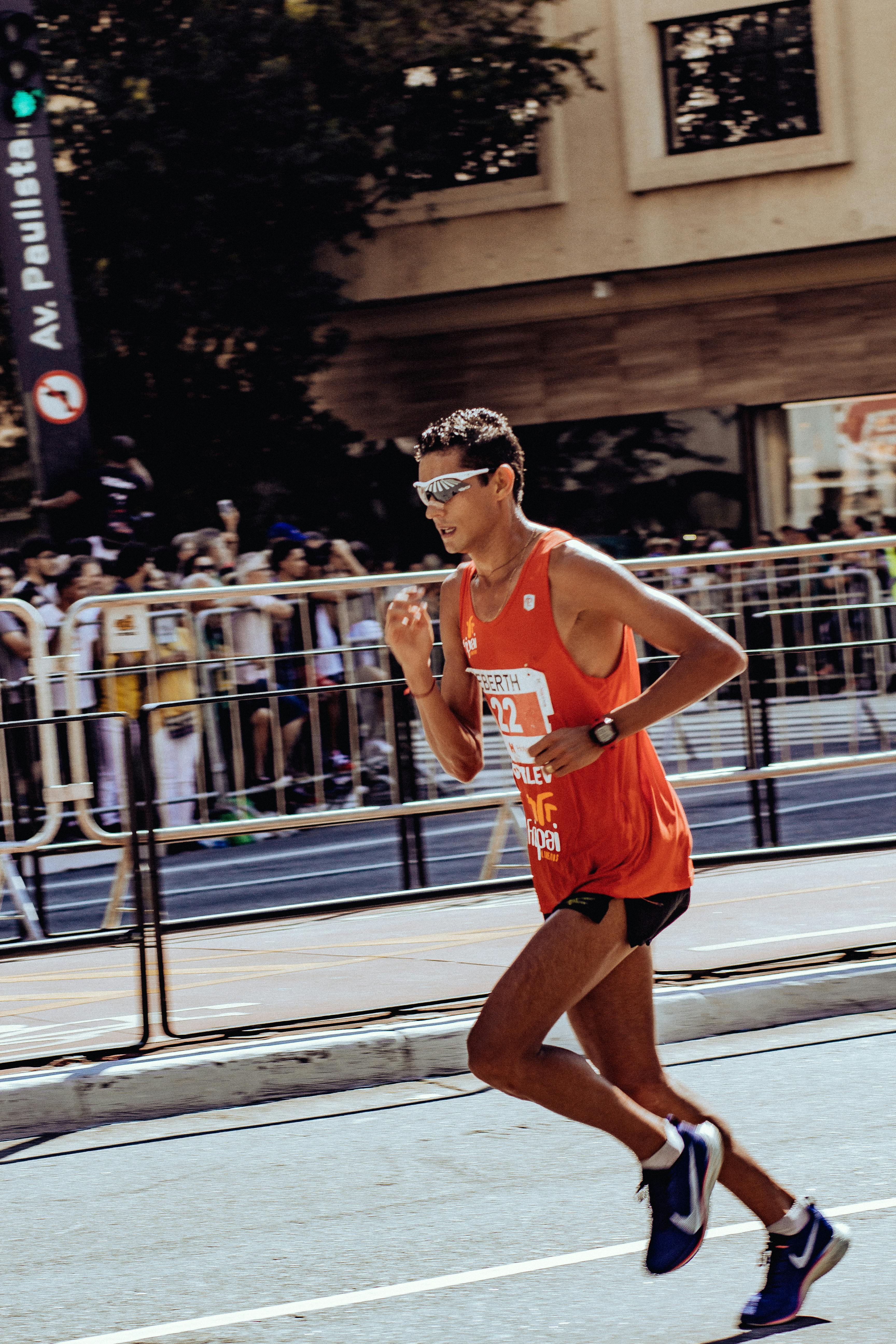 Marathon runner in motion during a road race, wearing an orange tank top on a sunlit street