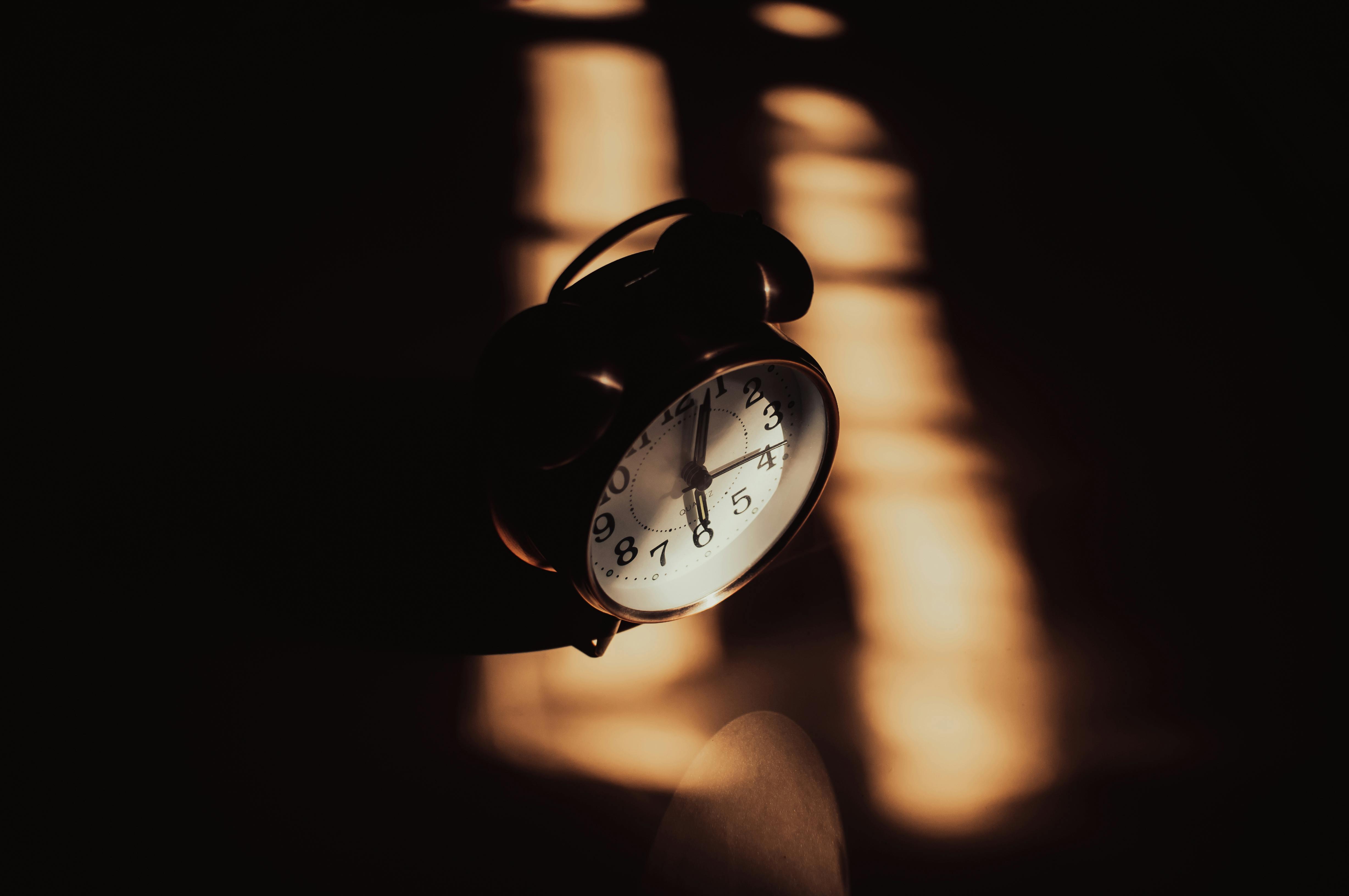 Retro analog alarm clock in moody shadows and warm lighting, evoking circadian rhythm disruption