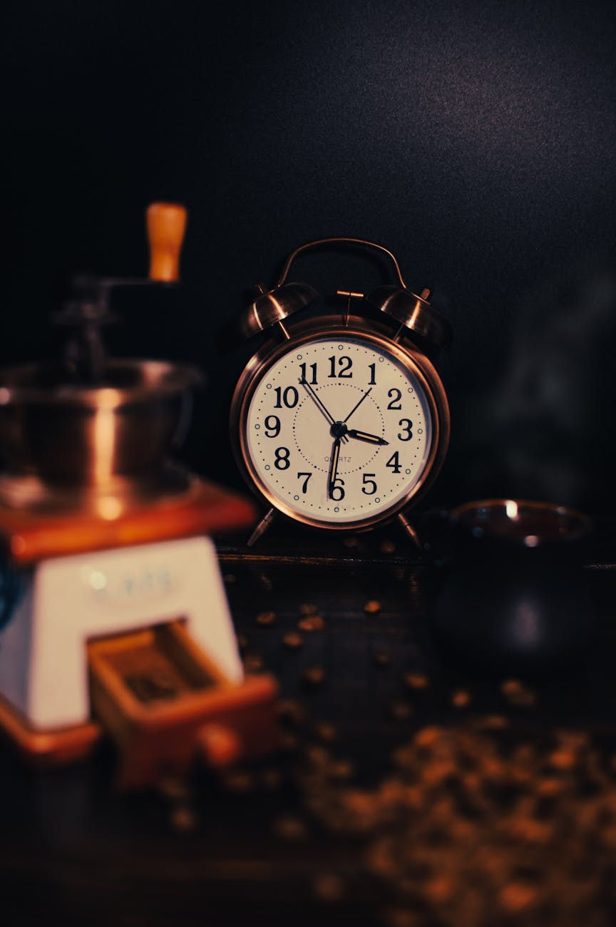 Vintage alarm clock surrounded by coffee beans and a grinder in warm lighting, visualising the relationship between caffeine consumption and sleep timing