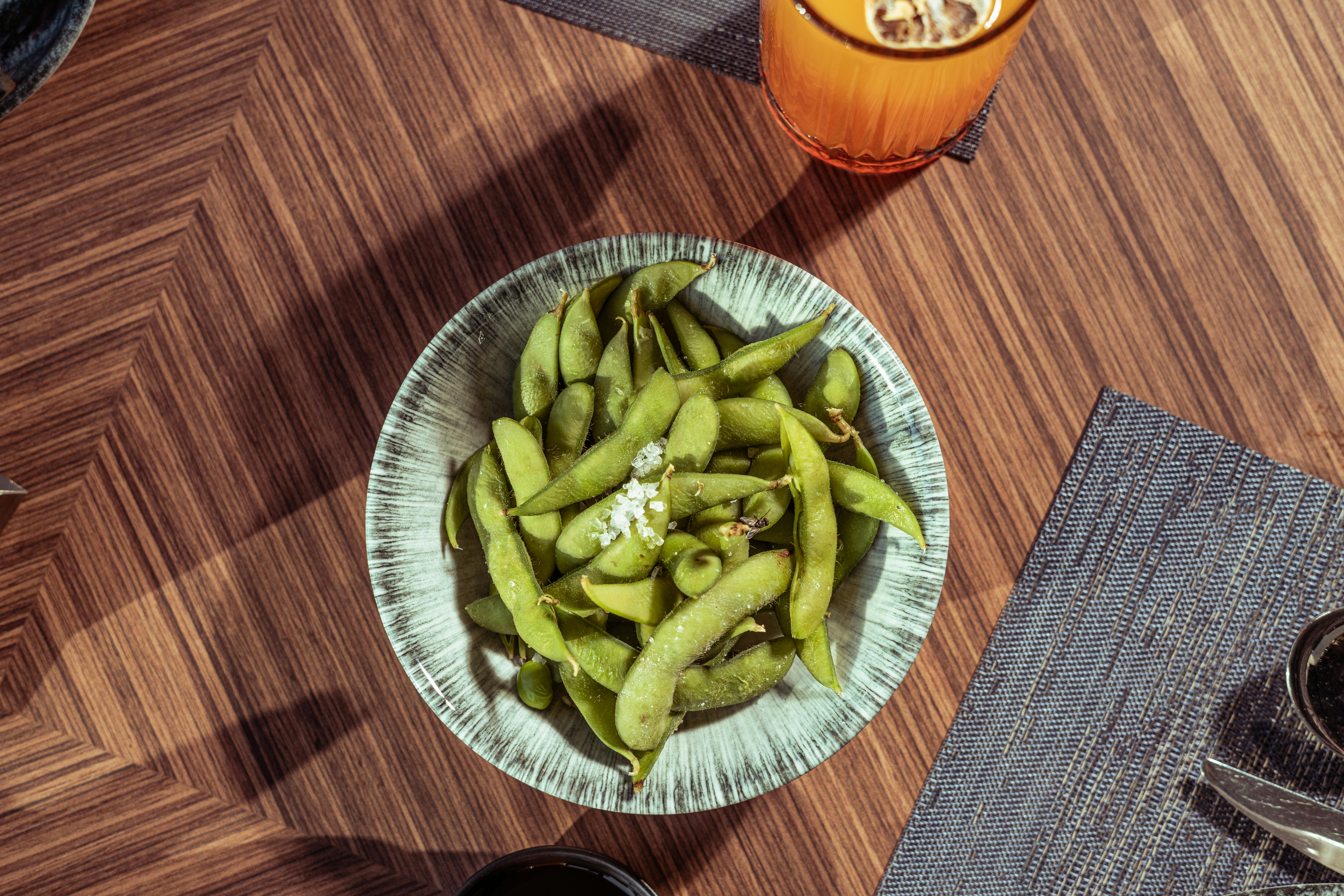Fresh edamame soybeans in a bowl with sea salt on a wooden table — whole soybeans are the richest dietary source of daidzein, genistein, and glycitein, the three isoflavones linked to hot flash reduction in the 2025 trial