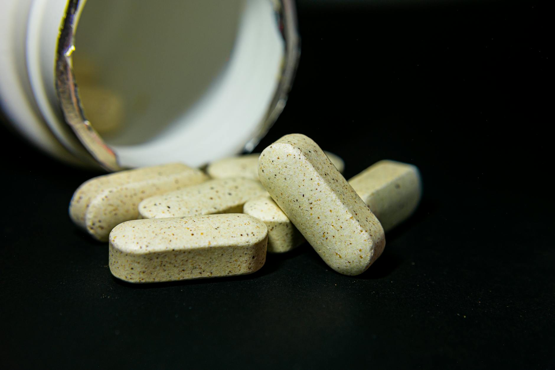 Close-up of white capsules spilled from a supplement bottle on a dark background