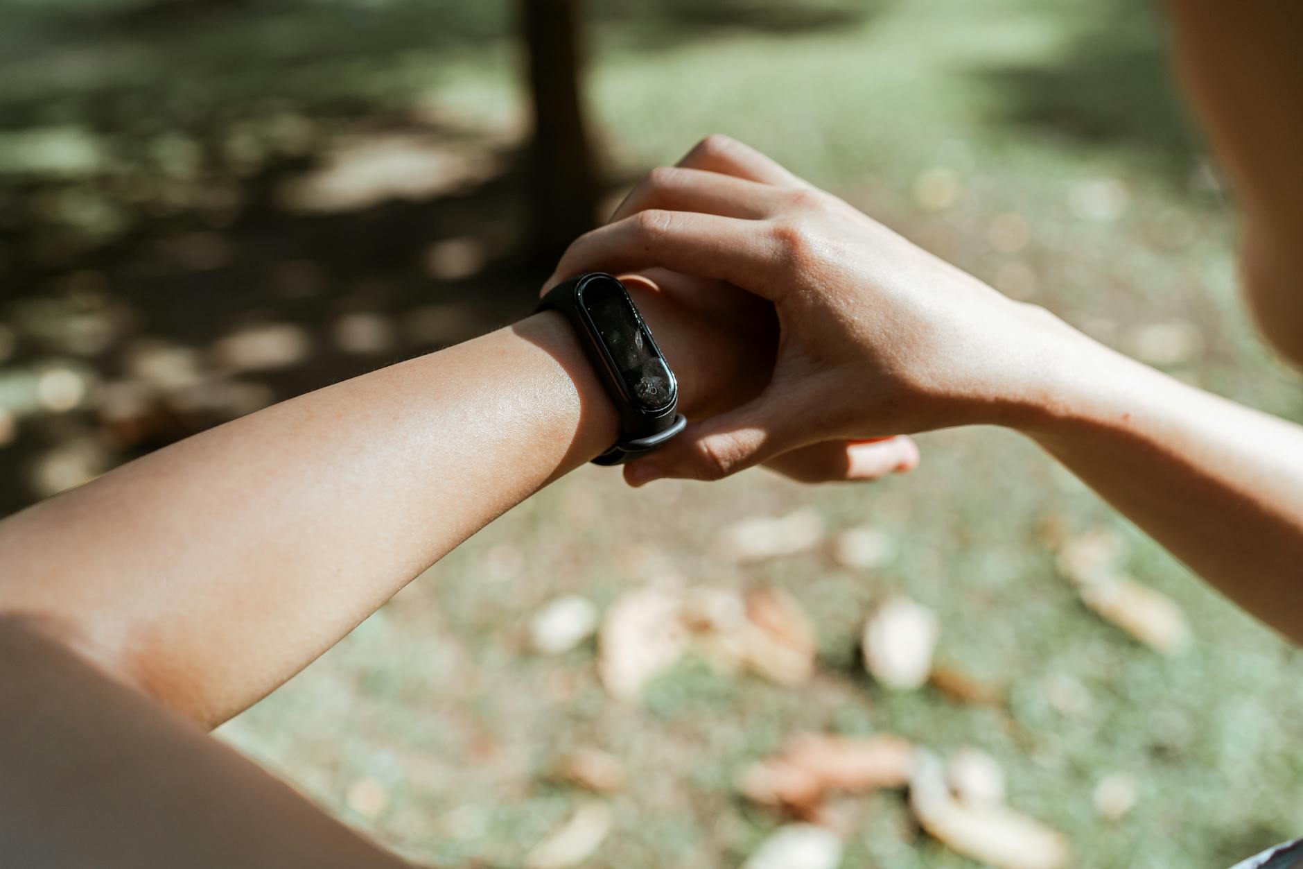 Close-up of a person wearing a black screenless fitness wristband outdoors in autumn, demonstrating the minimalist form factor of display-free health trackers
