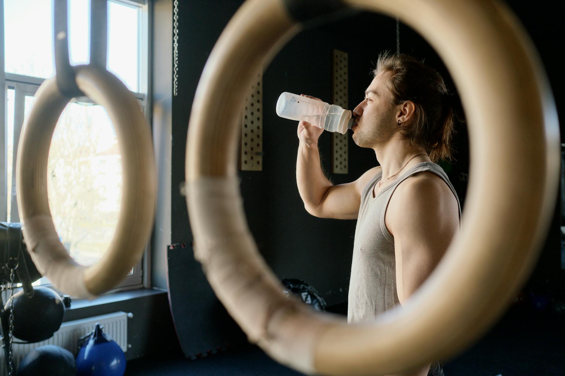 Athletic man drinking water in a gym after exercise.