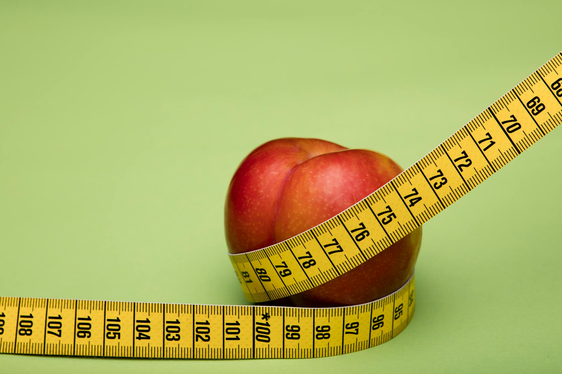 Green apple wrapped with a measuring tape against a clean green background