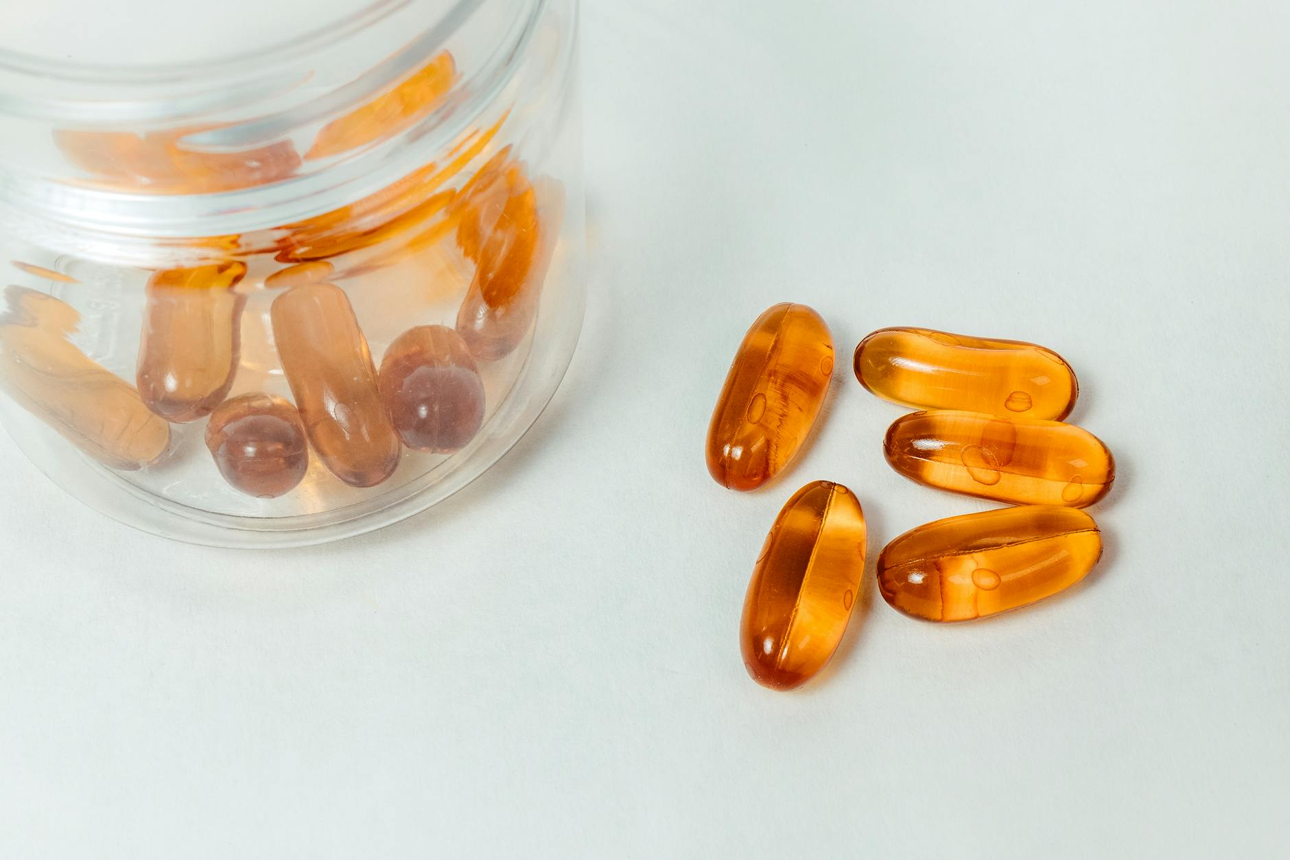 Amber vitamin capsules spilling from a glass jar on a white surface