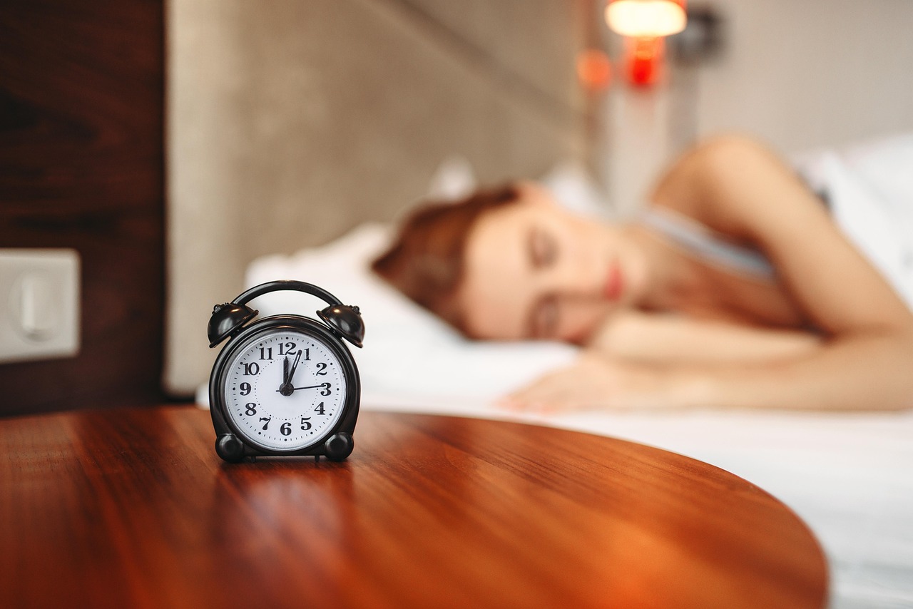 Alarm clock beside a bed, illustrating sleep timing and circadian rhythms.